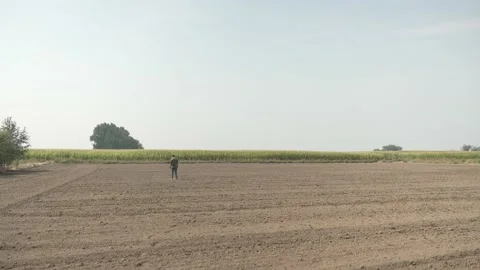 Wide shot farmer walks in empty farm field of plowed dirt to inspect the soil Stock-Footage 165471447