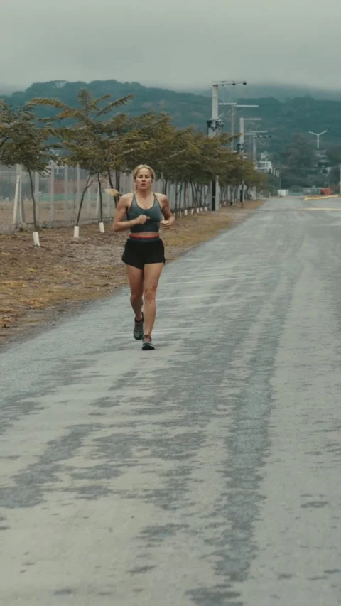 Wide shot of female runner approaching down open road toward hills Stock Footage 340046911