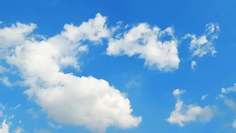 Wide shot of fluffy white clouds drifting across a clear blue sky background. Video stock 319340568