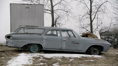 Wide shot of grey classic station wagon car abandoned in snow covered field Stock Footage 89945077