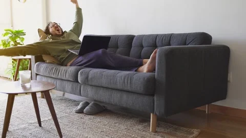 Wide shot of guy waking up after nap while working with laptop on the sofa Stock Footage 164905096