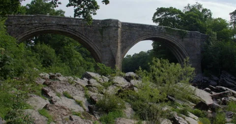 Wide shot looking up to devils bridge from the river Lune with rocks in Stock Footage 328655531