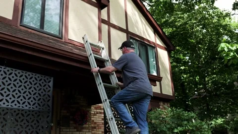 Wide Shot of Man Approaching and Climbing a ladder to clean his gutter Stock Footage 337603886