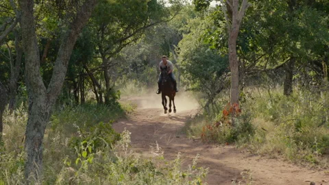 Wide shot of man cantering a horse along a dusty track Stock Footage