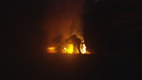 Wide Shot of a Man Furiously Digging a Hole in Front of a Blazing Fire Stock Footage 208779936