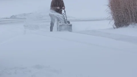 Wide shot of man pushing snow blower from the front, shooting snow to the side.  Stock Footage 86571008