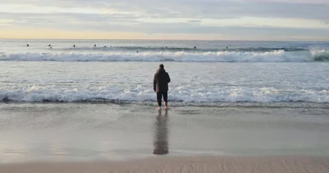 Wide shot of a man standing in the ocean watching surfers during sunrise 01 Stock Footage 137624979