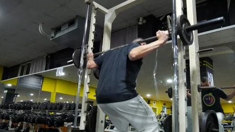 Wide shot of a man using the Smith machine at the gym to do weighted squats Stock Footage 102819338