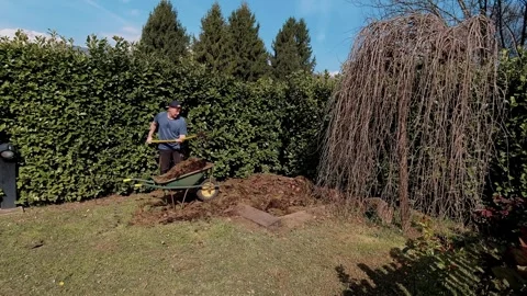 Wide shot of man working with pitchfork and compost near large humus pile in Stock Footage 332155200