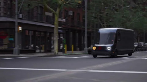 Wide shot of modern electric EV delivery van driving through streets of big city Stock Footage 238432244