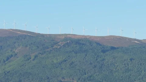 Wide shot of multiple wind turbines lined up along a mountain ridge above a Stock Footage 346712695
