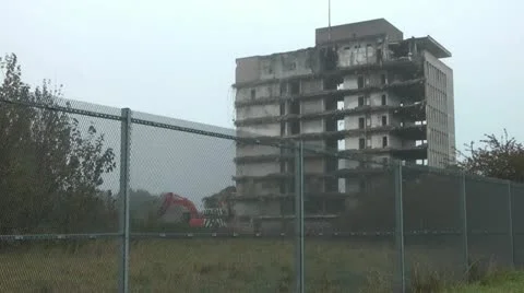 Wide shot of old tower block during demolition, digger works behind fence. Stock Footage