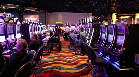 WIDE SHOT OF PEOPLE PLAYING ROWS OF SLOT MACHINES AT CASINO Stock Footage 59923134