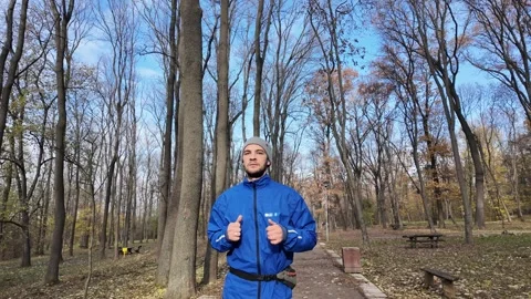 From wide shot to portrait view: man jogging in autumn park, wearing blue jacket Stock Footage 316837155