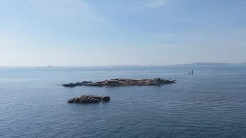 Wide shot of a rocky islet surrounded by calm blue sea under a clear sky, with Stock Footage 346723114