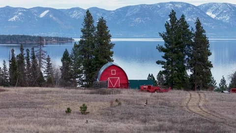 Wide shot of a rustic red barn set on open land overlooking a tranquil lake Stock Footage 332813189