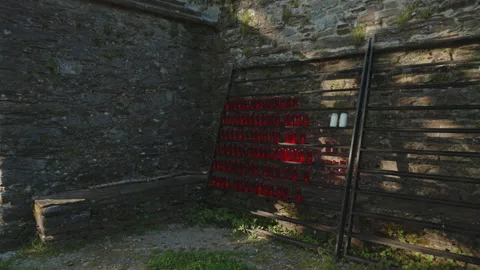 Wide shot showing a rustic stone wall with a candle rack featuring red votive 動画素材 344210431