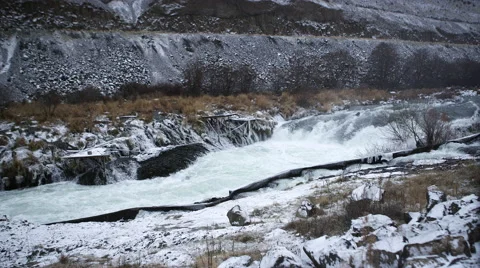 Wide shot in slow motion of a river rushing next to a snow and ice covered Видео 43794464