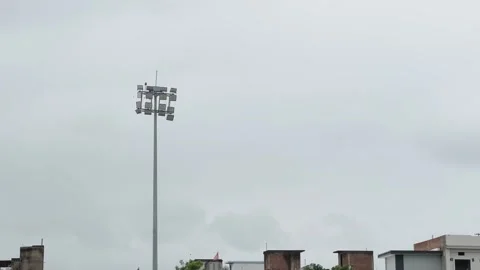 Wide Shot of Stadium Floodlight Tower Against Overcast Sky and Urban Buildings Stock Footage 344582891
