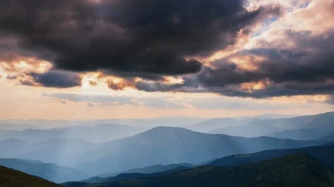 Wide shot of sun rays emerging through the dark storm clouds in the mountains Stock Footage