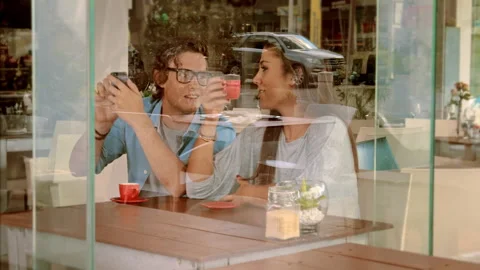 Wide shot through window of young couple using smart phone in cafe. Stock Footage 199634458