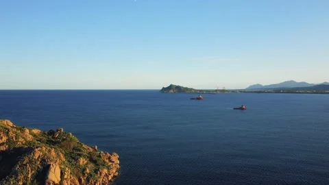 Wide shot of two boats on the deep blue sea with rocky coastline in the Stock Footage 346698995