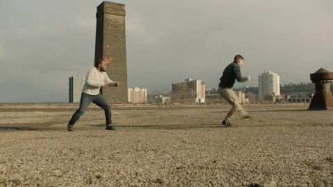 Wide shot of two men fighting on a warehouse rooftop with skilled kicks and punc Stock Footage 199459055