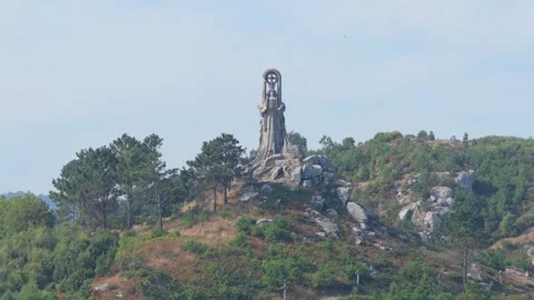 Wide shot of the Virxe da Rocha monument standing atop a rocky, green hill Stock Footage 346672181