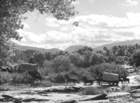 Wide shot of wagon train crossing stream, 1930s Stock Footage 260258533