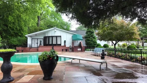 Wide shot of wet pool deck and white house with green awning Stock Footage 336351875