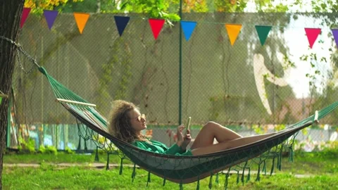 Wide shot of Woman is lying on a hammock and searching the internet on her p Stock Footage 203510053