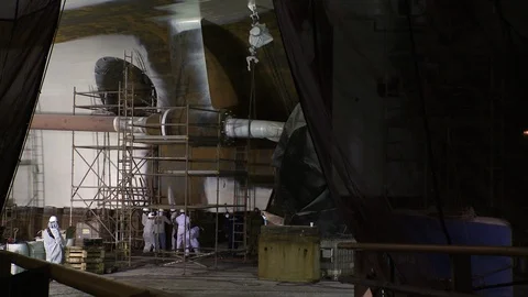 Wide shot of workers spray painting ship hull in construction harbor Stock Footage 123728921