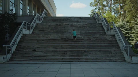 Wide shot of a young boy running up a massive concrete staircase. 動画素材 343209687