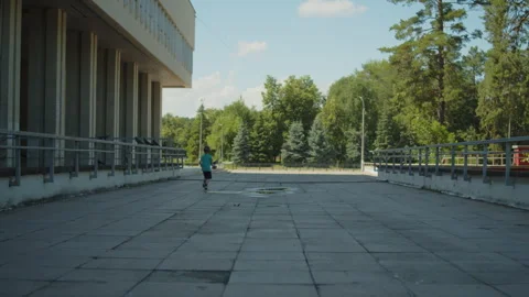 Wide shot of a young boy running across a plaza and scaring of pigeons. Video stock 343210428