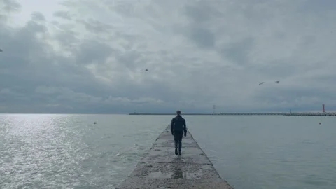 Wide shot of young guy walks on a pier from the camera at sunny day Stock Footage 151078112