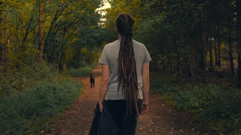 Wide shot of young man with dreadlocks walking his dog in the woods. Stock Footage 96635788