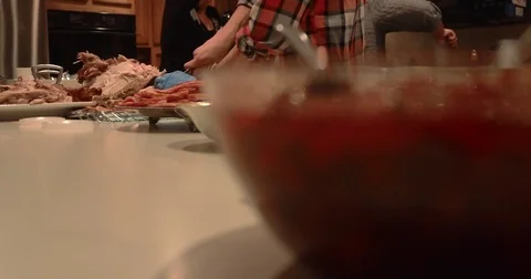 Wide Shot of Young Man Preparing Turkey in the Kitchen Surrounded by Family Stock Footage 83488383