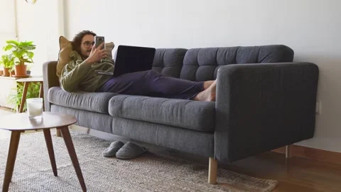 Wide shot of young man on the sofa taking selfie while using laptop Stock Footage 164905571