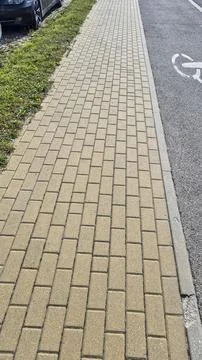 Wide sidewalk featuring interlocking brick patterns, bordered by green grass and Stock Photos
