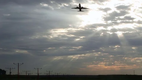 Wide of a silhouetted airplane taking off in front of a sunrise cloudscape Stock Footage 80439858