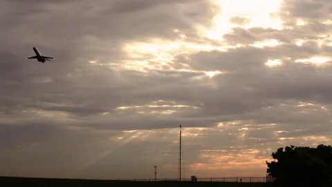 Wide of a silhouetted airplane taking off in front of a sunrise cloudscape Stock Footage 80439891