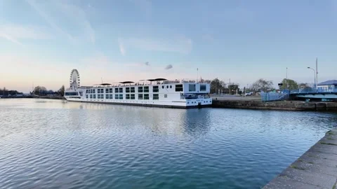 Wide static shot over calm river waters reflecting a pastel sunset and a moored Vídeos de archivo 332860881