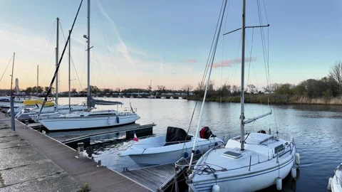 Wide static shot of yachts and a small motorboat docked in a calm marina at suns Vídeos de archivo 332860928