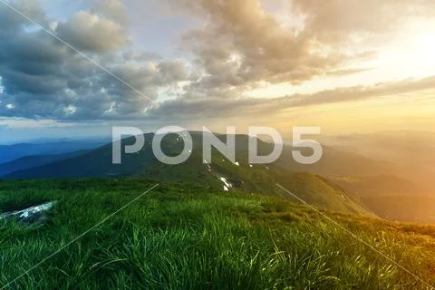 Wide summer mountain view at sunrise. Glowing orange sun raising in blue clou Stock Photos