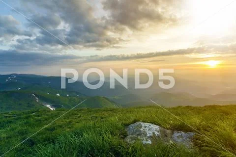 Wide summer mountain view at sunrise. Glowing orange sun raising in blue clou Stock Photos