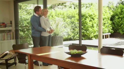 Wide, Track shot happy couple emracing in modern house in front of window Stock Footage