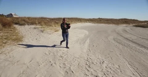 Wide tracking shot of lady using a tablet walking on the beach Stock Footage 71145737