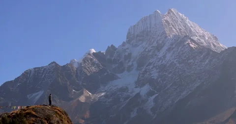 Wide tracking shot of a man running on a mountain cliff edge against Mount Stock Footage 337394368