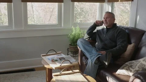 Wide tracking shot of an older man relaxing in a sunroom talking on the phone Stock Footage 70809809