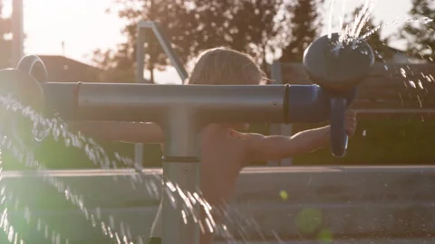 Wide view of 3 year old boy playing with yellow water gun at splash pad Stock Footage 233946161